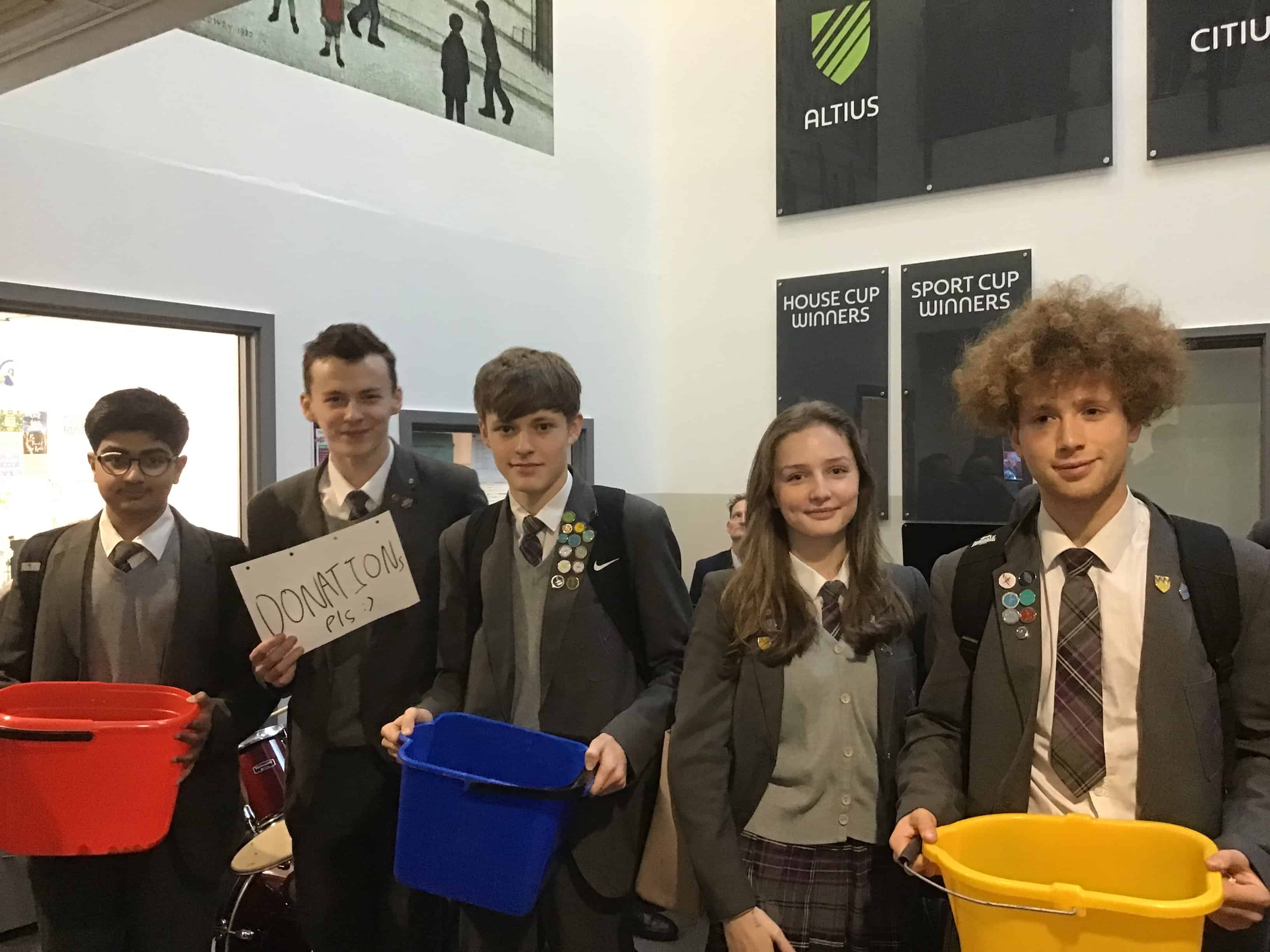 Students at Laurus Cheadle Hulme hold up buckets for donations.